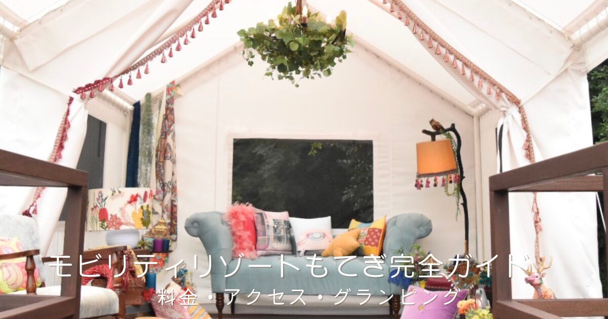 白いグランピングテントの内観。三角の天井からグリーンを飾ったシャンデリアが下がり、中央にはくすみブルーのヴィンテージソファとカラフルなクッション、足元にはエスニック柄のラグが敷かれた、華やかでボヘミアンな空間。「モビリティリゾートもてぎ完全ガイド｜料金・アクセス・グランピング」の文字入り。栃木県茂木町のリゾート施設（旧ツインリンクもてぎ）を紹介するおでかけガイド記事のアイキャッチ画像。