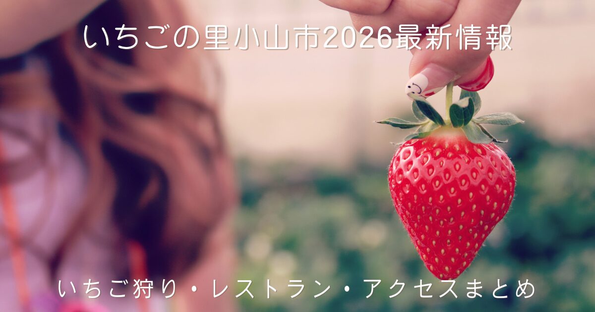女性が指先で大きく赤いいちごを1粒つまんでいる写真。背景はいちご狩りハウス。栃木県小山市「いちごの里」2026年最新のいちご狩り・レストラン・アクセス情報をまとめた記事のアイキャッチ画像。